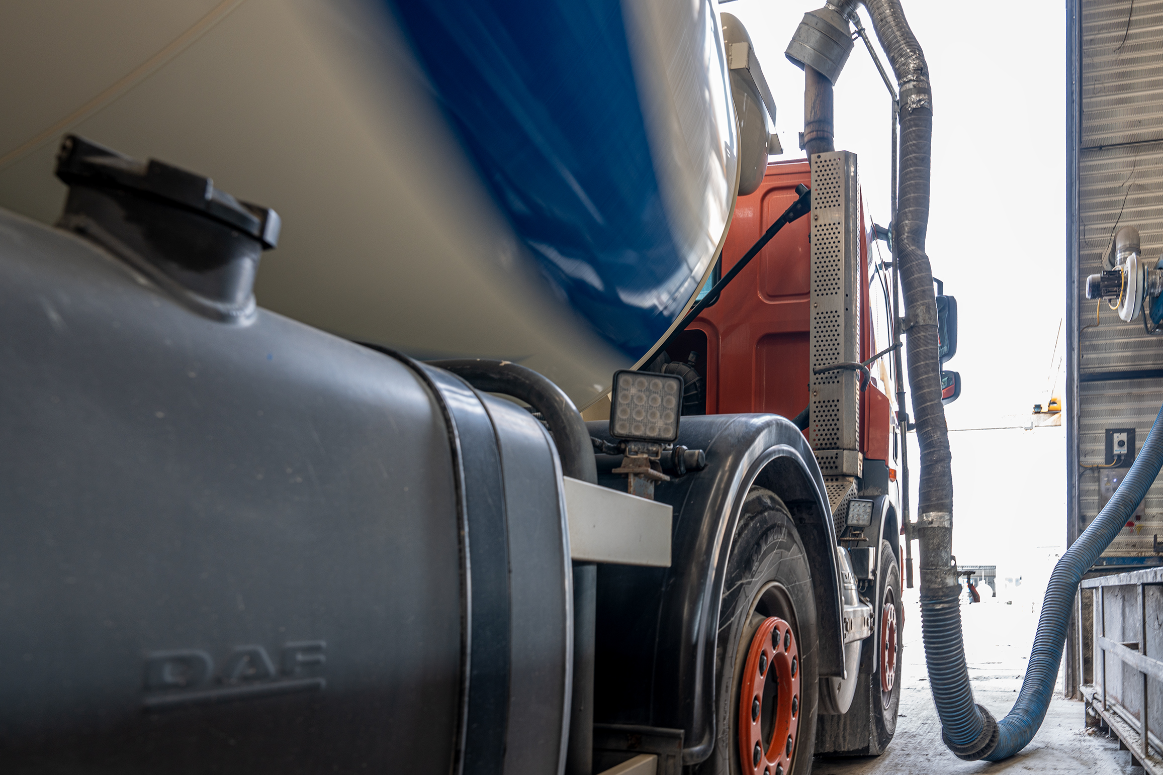 Close-up van een industriële DAF-vrachtwagen met aangesloten slangen en een grote tank, gebruikt bij funderingswerkzaamheden.